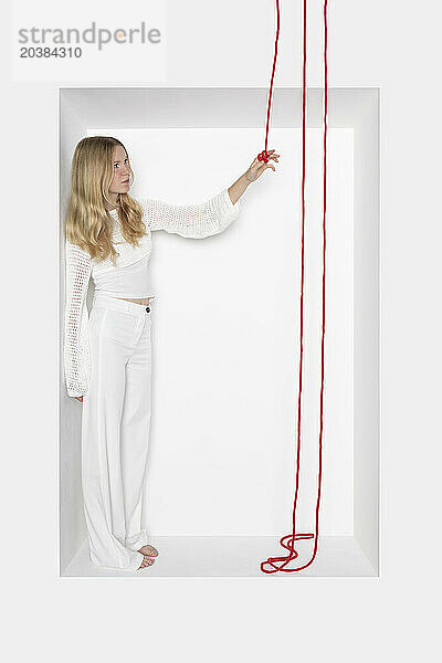 Teenager holding thread standing in alcove against white background