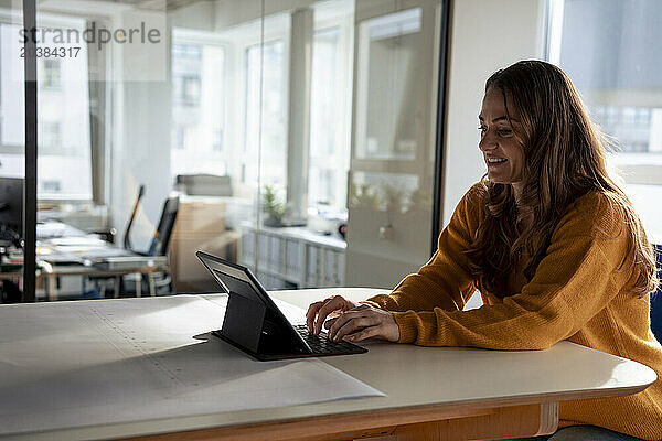 Smiling businesswoman typing on keyboard and using tablet PC in office