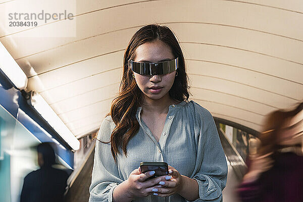 Woman wearing smart glasses and using smart phone at subway station