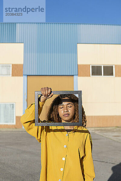 Young woman with eyes closed holding picture frame on sunny day