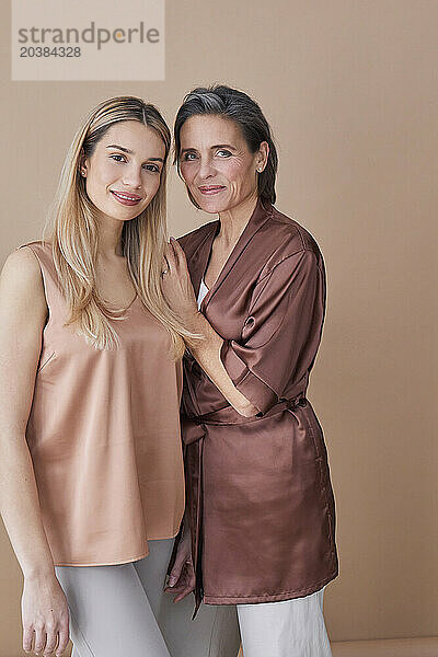 Beautiful mother and daughter standing against beige background