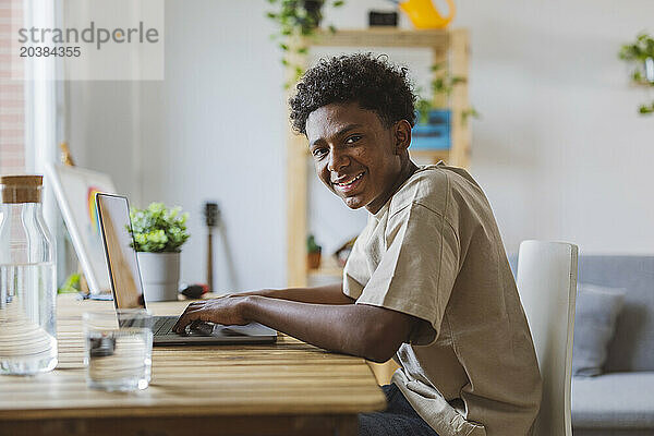 Happy teenage boy using laptop at home