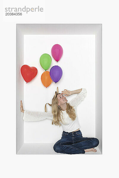 Teenager with colorful balloons sitting in alcove against white background