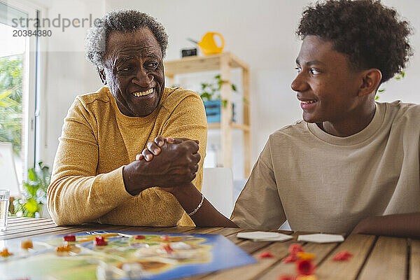 Smiling grandson holding hand of grandfather while playing board game at home