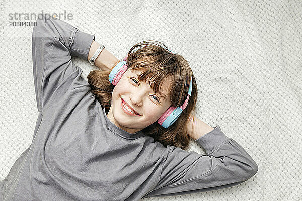 Smiling girl listening to music with hands behind head at home