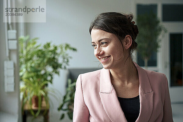 Smiling businesswoman wearing blazer looking away at home office