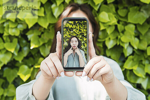 Woman showing picture on smart phone near hedge