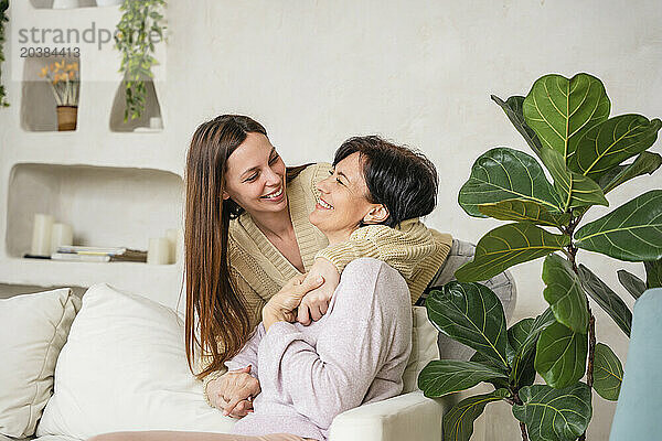 Happy woman embracing mother siting on sofa at home