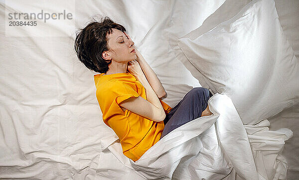 Woman in yellow t-shirt sleeping by pillow on bed at home