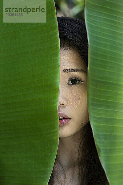 Young woman hiding behind banana leaves