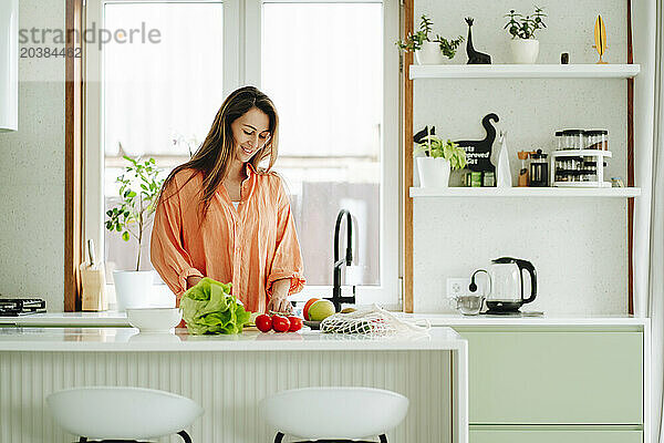 Smiling woman with long hair preparing food in kitchen at home