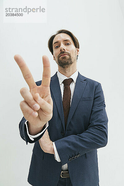 Confident mature businessman showing victory sign against white background