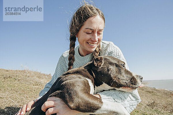 Smiling woman spending leisure time with dog on hill at sunny day