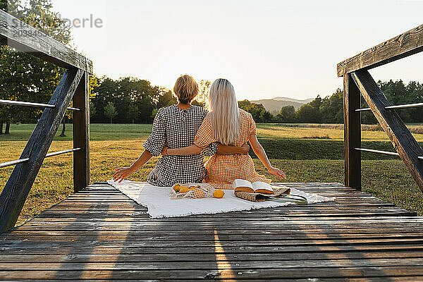 Women with arms around sitting on boardwalk in park