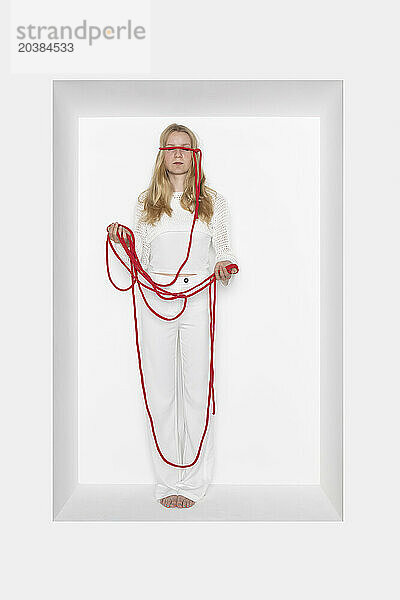 Teenage girl with thread tied on eyes against white background