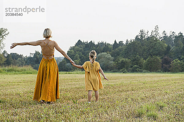 Mother holding hand of daughter and walking in meadow