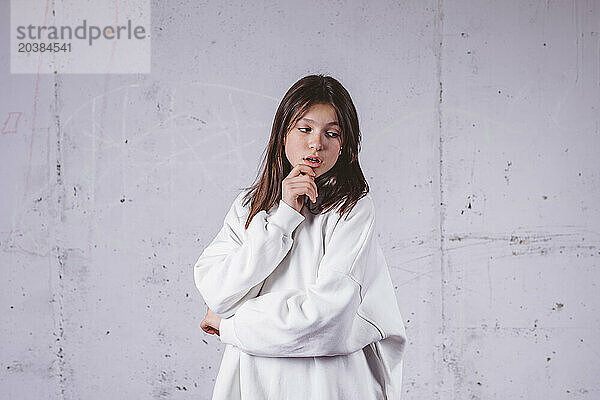 Girl in white hoodie posing in front of gray cement background