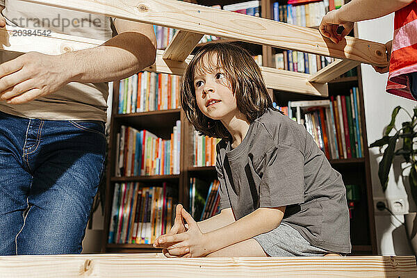 Boy inside of wooden furniture by father and sibling at home