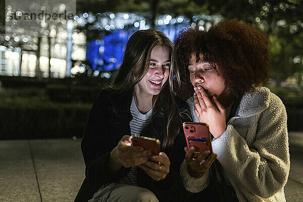 Happy friends sharing smart phones at night