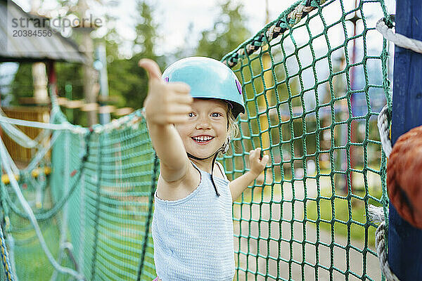 Excited smiling girl showing thumbs up gesture near net at rope park