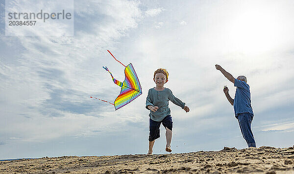 Playful boy with grandfather flying kite at beach