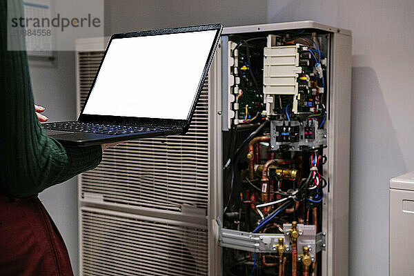 Engineer holding laptop and standing near network server in office