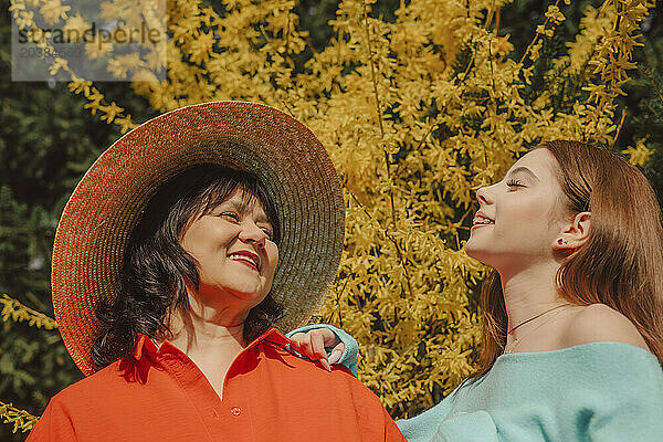 Happy mother and daughter enjoying sunlight near yellow blossom tree