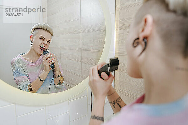 Passionate woman singing in bathroom holding electric razor