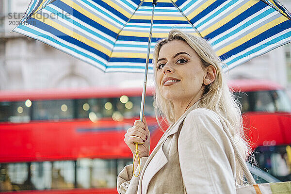 Happy young woman with umbrella near red bus