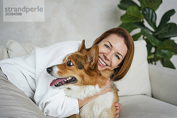 Happy woman embracing dog on sofa at home