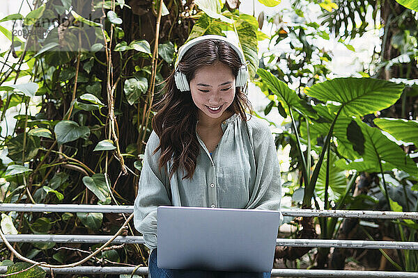 Smiling woman wearing wireless headphones and using laptop