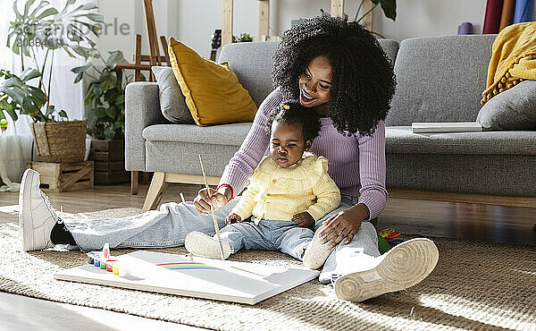 Happy mother painting rainbow sitting with daughter on carpet in living room