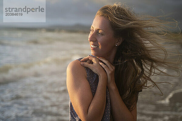 Smiling blond woman enjoying sunset at windy beach