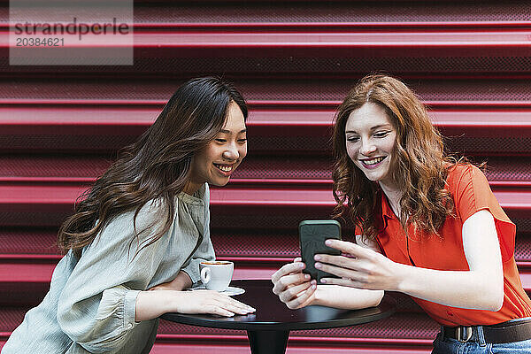 Smiling woman sharing smart phone with friend near shutter