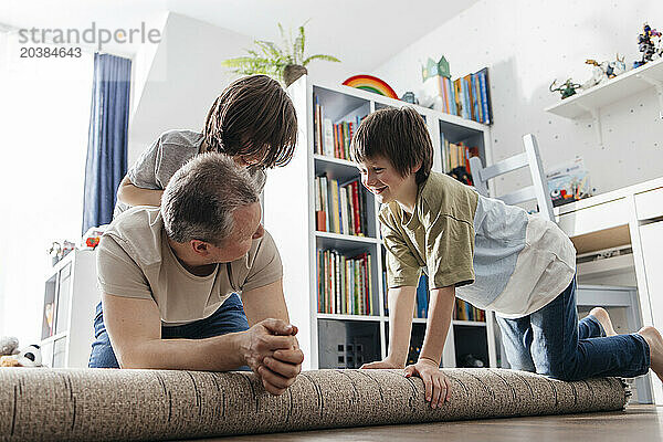 Happy children playing with father on rolled up carpet at home