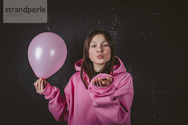 Girl puckering and holding pink balloon in front of black background