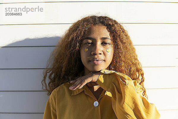 Curly haired woman with heart stickers on cheek in front of white shutter