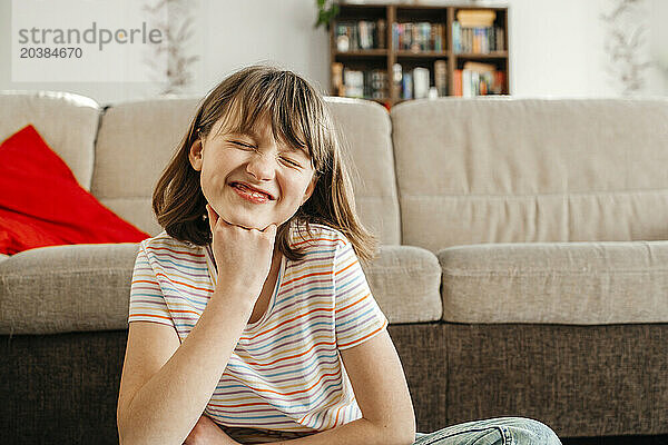 Smiling boy with hand on chin sitting near sofa at home