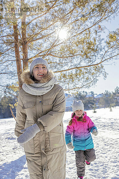 Mother and daughter running in winter forest on sunny day