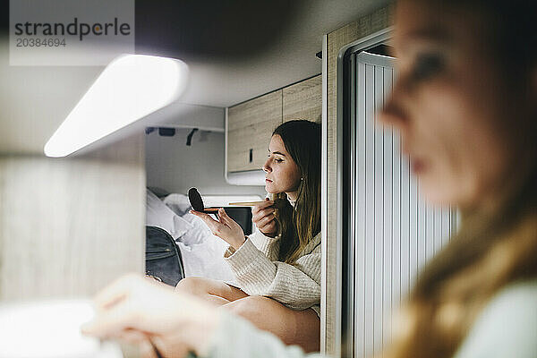 Woman applying make-up looking at hand mirror