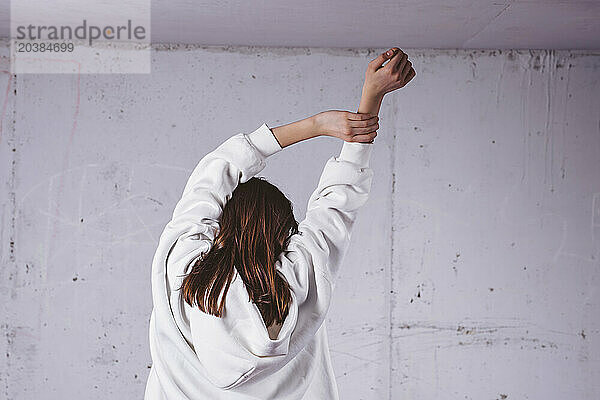 Girl with arms raised in front of gray cement wall