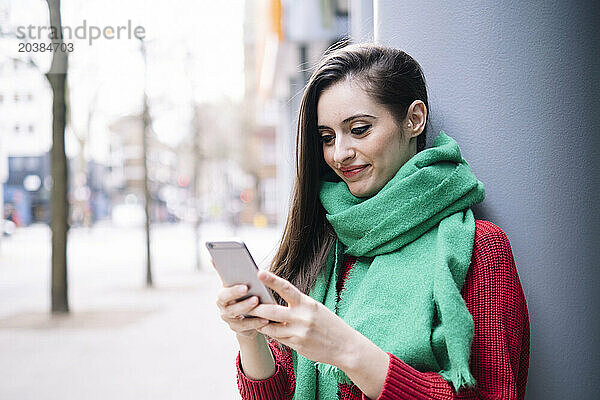 Smiling woman using smart phone near column on street