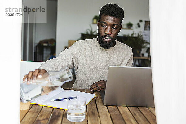 Freelancer pouring water in glass near laptop at desk