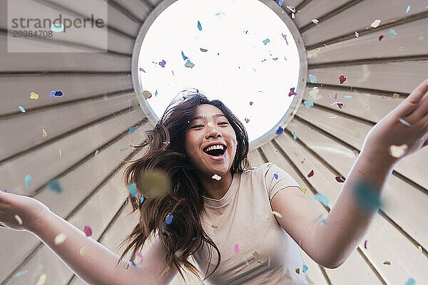 Cheerful woman playing with colorful confetti under canopy