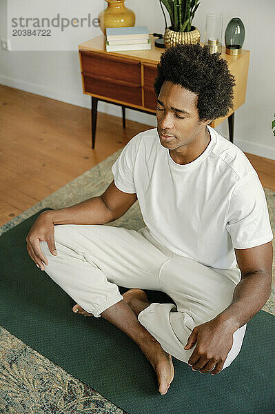 Man on exercise mat with eyes closed doing yoga in morning