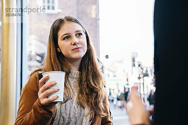 Young woman holding disposable cup at cafe
