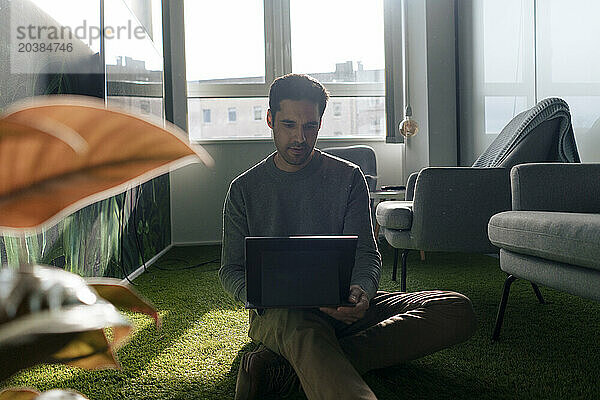 Businessman sitting on green carpet and using tablet PC in office