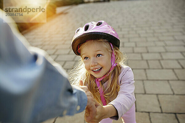 Smiling girl with helmet holding hand of father on footpath