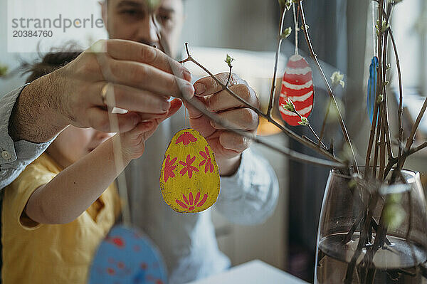 Father and son decorating painted Easter eggs on twigs