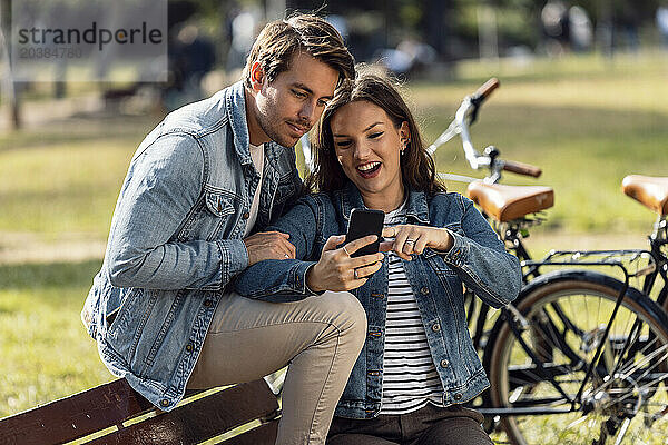 Happy woman showing smart phone to boyfriend at park